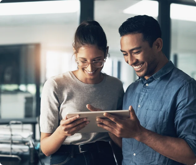 Duas pessoas da equipe sorrindo enquanto usam um tablet no escritório